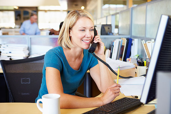 Une jeune femme au téléphone, assise à son bureau au travail